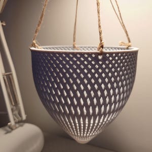 May include: A grey hanging planter made of a lattice design with a rope hanger.