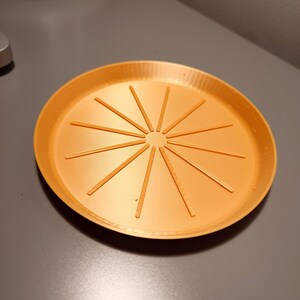 May include: Orange plastic saucer with a circular design of radiating lines.