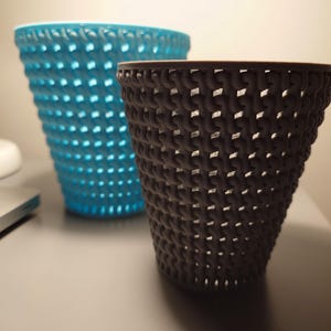 Könnte beinhalten: Zwei geflochtene Körbe, einer blau und einer grau, stehen auf einem Tisch. Die Körbe sind aus einem geflochtenen Material gefertigt und haben eine zylindrische Form.