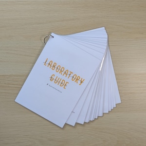 May include: A white, spiral bound laboratory guide with the text "LABORATORY GUIDE" in orange lettering and the text "@thebestnursellife" in black lettering.