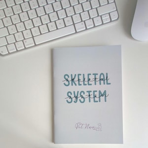 May include: A white notebook with the text SKELETAL SYSTEM printed in large blue block letters with thin black cursive script overlaid. At the bottom, a small logo features the text Vet Nurse Life with a simple line drawing of a dog head.