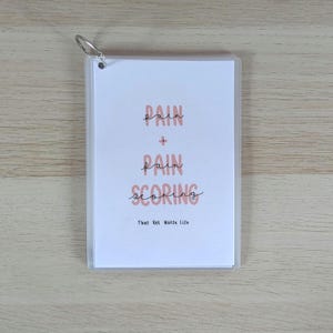 May include: A white ceramic mug with a black handle and the text "But First, Coffee" in a bold, black font. The mug is set against a blurred background. The mug appears to be approximately 10 cm tall.