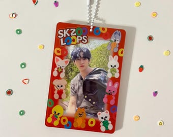 May include: Red plastic keychain with a photo of a person in a black leather jacket and a striped shirt. The keychain has a white frame with cartoon animals and the text "SKZOO LOOPS" in white letters.