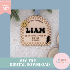 Può includere: Un ornamento in legno ad arco con bordo a scacchi, una faccina gialla sorridente con occhi a forma di fulmine e un fulmine nero. Il testo recita: MY FIRST CHRISTMAS, LIAM, 09 28 2006, 08:03 AM, 7 LB 2 OZ e 21 INCHES.