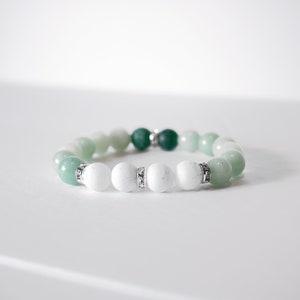 May include: A green and white beaded bracelet with silver accents. The bracelet is made with round beads and has a graduated color scheme, starting with dark green and transitioning to light green and white.