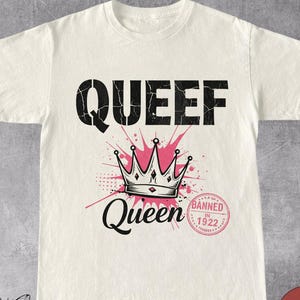 Pode incluir: Camiseta branca com texto preto que diz "Queef Queen" e uma coroa sobre um fundo rosa. O texto "Banned in 1922" está em um círculo abaixo da coroa.