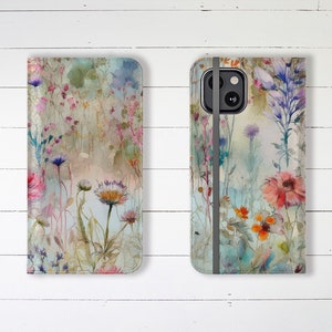 May include: A floral phone case and wallet case set. The cases feature a watercolor design of wildflowers in shades of pink, orange, blue, and purple. The cases are set against a white wooden background.