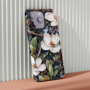 May include: A black phone case with a floral design featuring white magnolia flowers and green leaves. The case has a camera cutout with three lenses.