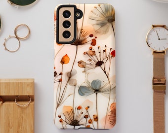 Peut inclure: Une coque de téléphone blanche avec un motif floral composé de fleurs délicates, ressemblant à de l'aquarelle, dans des tons d'orange, de brun et de bleu. La coque a un découpage de caméra noir avec trois objectifs.