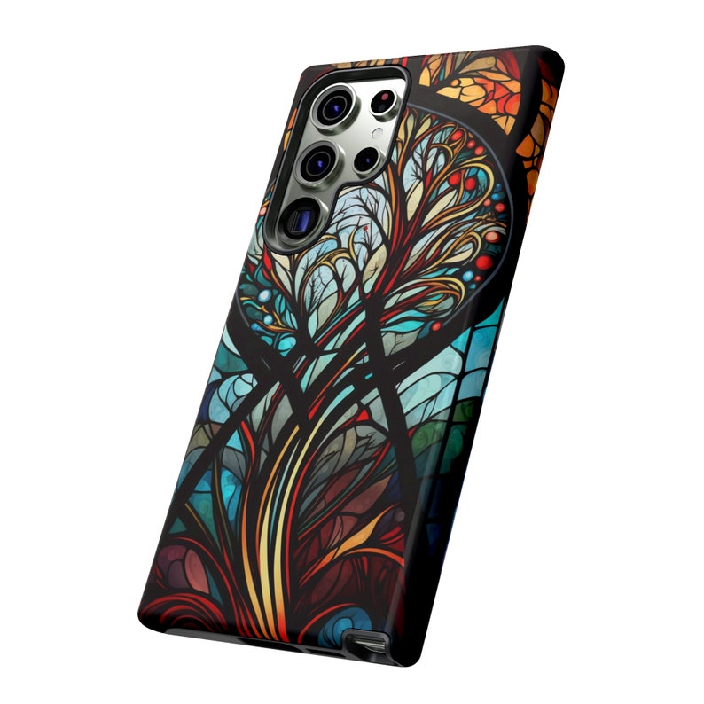 May include: A phone case with a colorful stained glass design featuring a tree with intricate branches and leaves. The case is black and has a cutout for the phone's camera.