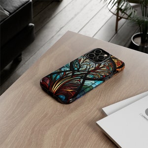 May include: A black phone case with a colorful stained glass design featuring a tree with intricate branches and leaves. The case has a cutout for the phone's camera lenses.
