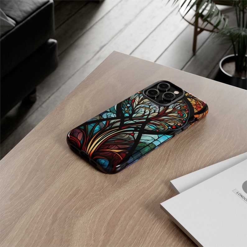 May include: A black phone case with a colorful stained glass design featuring a tree with intricate branches and leaves. The case has a cutout for the phone's camera lenses.