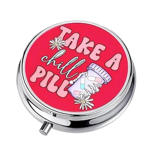 May include: A round, silver pill case with a red top. The top features the phrase "TAKE A chill PILL" in pink and white lettering, along with a cartoon illustration of a pill bottle and flowers.