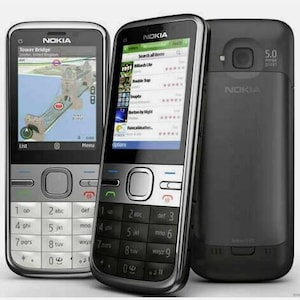 May include: Three Nokia mobile phones. One displays a map of Tower Bridge, London. Another shows a list of apps. The third phone is black with a camera and the text "5.0 mega pixel". The phones have silver and black accents.