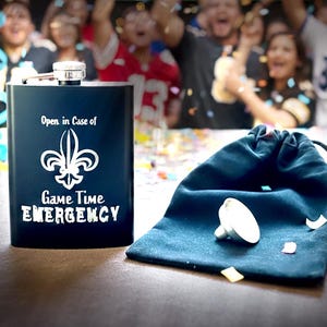 May include: A black flask with a silver cap and the text "Open in Case of Game Time Emergency" and a fleur-de-lis logo. A blue drawstring bag and a silver bottle stopper are next to the flask. Confetti and cheering fans are in the background.