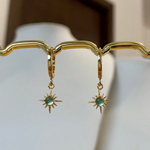 Puede incluir: Un par de pendientes de aro de oro con un colgante de estrella. Cada estrella tiene una piedra preciosa verde claro en el centro.