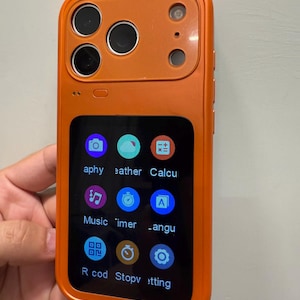 May include: Orange smartphone with a rectangular screen displaying app icons. The phone has a camera array on the top left and a single camera on the top right. The screen displays icons for a camera, weather, calculator, music, timer, language, record, stopwatch, and settings.