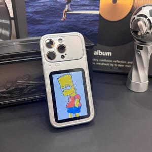 May include: Silver phone case with a screen displaying Bart Simpson in a red shirt and blue shorts. The case has multiple camera lenses and a sleek design. The background includes an album cover and other decorative items.