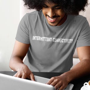 Puede incluir: Una persona con una camiseta gris con el texto "Intermittent Connectivity" impreso en la parte delantera, usando un ordenador port&aacute;til.