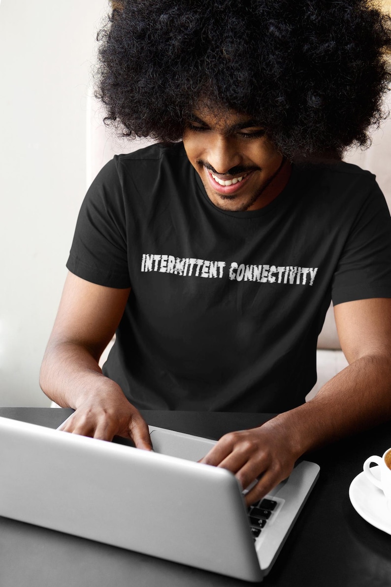 Puede incluir: Una persona con una camiseta negra con el texto "Intermittent Connectivity" en blanco. La persona est&aacute; sentada en una mesa y usando una computadora port&aacute;til.