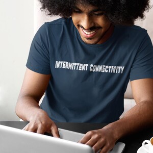 Puede incluir: Una persona lleva una camiseta azul marino con el texto "INTERMITTENT CONNECTIVITY" en letras blancas. La persona est&aacute; usando una computadora port&aacute;til plateada.