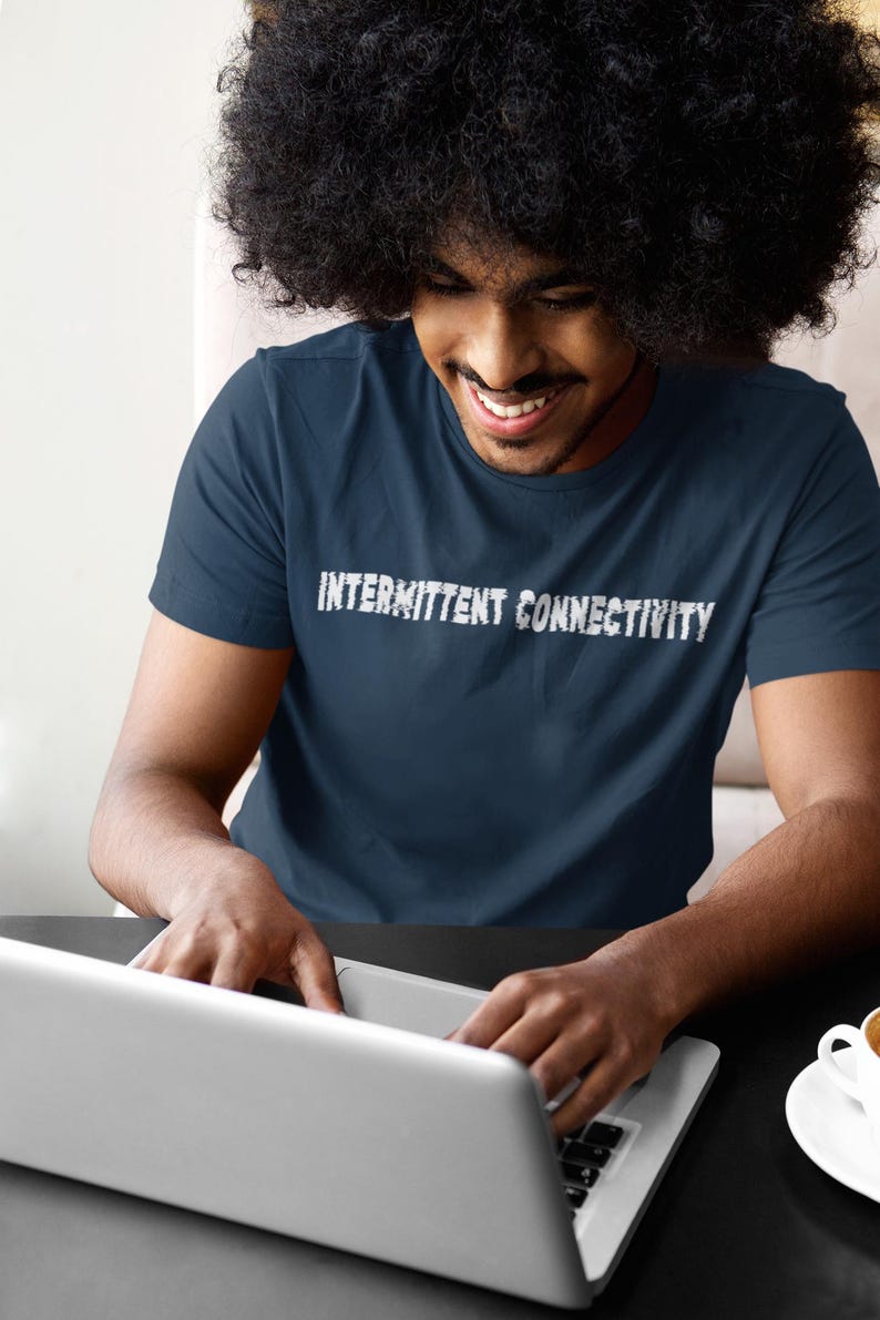 Puede incluir: Una persona lleva una camiseta azul marino con el texto "INTERMITTENT CONNECTIVITY" en letras blancas. La persona est&aacute; usando una computadora port&aacute;til plateada.