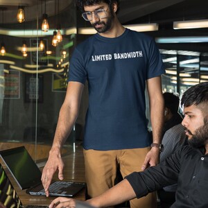 Pode incluir: Duas pessoas trabalhando em uma mesa com laptops. Uma pessoa est&aacute; vestindo uma camiseta azul marinho com o texto "Limited Bandwidth" impresso nela. A outra pessoa est&aacute; vestindo uma camisa preta de bot&otilde;es.