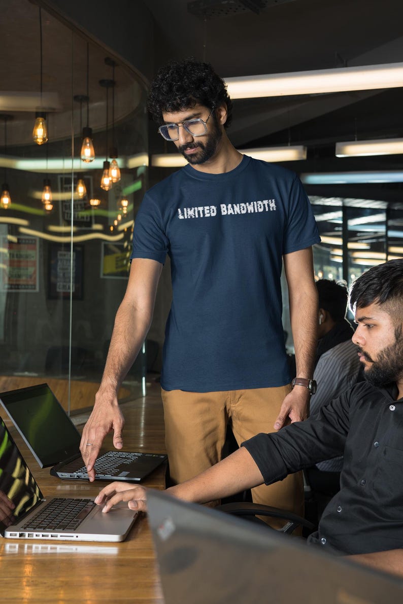 Pode incluir: Duas pessoas trabalhando em uma mesa com laptops. Uma pessoa est&aacute; vestindo uma camiseta azul marinho com o texto "Limited Bandwidth" impresso nela. A outra pessoa est&aacute; vestindo uma camisa preta de bot&otilde;es.