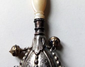 May include: An antique silver perfume bottle with a pearlescent stopper. The bottle has ornate floral and beaded detailing. A small, gold-toned decorative element hangs from the side. Likely from the Victorian era.