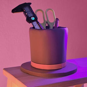Könnte beinhalten: Ein brauner Hut-förmiger Schreibtisch-Organizer mit einem schwarzen Band und einem rosafarbenen Rand. Der Organizer enthält eine gelbe Schere, einen Stift und eine schwarze digitale Schieblehre mit einer digitalen Anzeige, die "0.3" anzeigt.