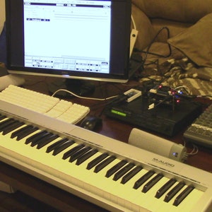 May include: A white MIDI keyboard with black keys and a blue light on the left side. The keyboard is labeled "M-AUDIO Keystation 49e".