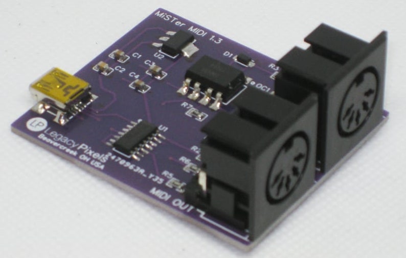 May include: A purple circuit board with the text "MiSTer MIDI 1.3" and "Legacy Pixels" printed on it. The board has two black MIDI connectors, a USB connector, and various electronic components.