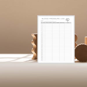 May include: A white Blood Pressure Log with a heart icon is displayed. The log has columns for recording data. Wooden decorative shapes are arranged around the log on a neutral surface.