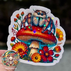 Könnte beinhalten: Ein farbenfroher Sticker mit einer Springspinne, die auf einem roten und weißen Pilz mit blauem Stiel sitzt. Der Pilz ist von verschiedenen Blumen in Rot-, Gelb- und Orangetönen umgeben. Der Sticker hat eine holografische Oberfläche, die einen schimmernden Effekt erzeugt.