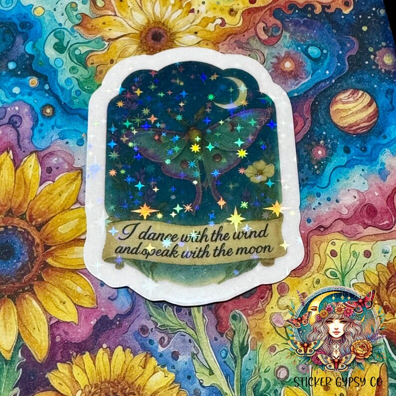 A holographic vinyl sticker featuring a glowing Luna moth beneath a crescent moon is placed on a vibrant cosmic floral background. The design includes lavender, yellow flowers, and a starry night sky, accented by shimmering rainbow holographic stars. The quote “I dance with the wind and speak with the moon” is written on a golden scroll banner at the bottom. Surrounding the sticker are vivid watercolor-style sunflowers and swirling galaxies.