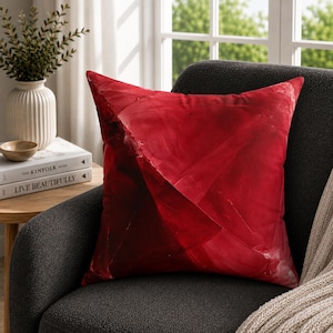 May include: A square throw pillow featuring a deep red color palette with abstract, layered geometric shapes and subtle tonal variations. The surface displays a smooth texture with darker crimson shadows and lighter scarlet highlights across the fabric.