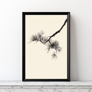 May include: A framed wall art print featuring a black ink illustration of a pine tree branch with needle clusters. The artwork is set against a solid cream-colored background and enclosed within a thin, black rectangular frame.