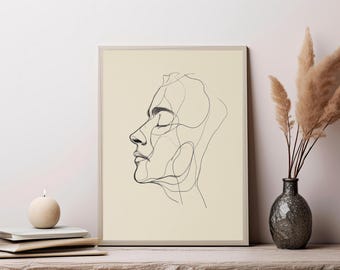 May include: A rectangular framed wall art print featuring a black continuous line drawing of a human face in profile on a cream-colored background. The artwork depicts the side view of a head with closed eyes and defined facial features.