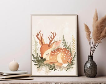 May include: A framed wall art print featuring a watercolor illustration of a young deer with antlers resting among green ferns. The deer has light brown fur with white spots and closed eyes, set against a soft, neutral, cream-colored background.
