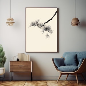 May include: A framed wall art print featuring a black ink illustration of a pine tree branch with needles against a solid cream background. The artwork is displayed in a dark brown frame, centered on a light gray wall above a wooden cabinet.