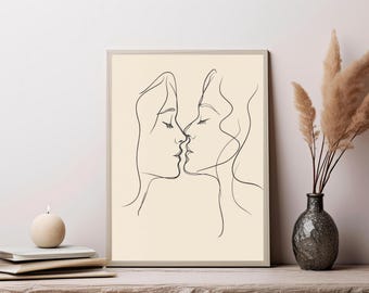 May include: A framed wall art print featuring a continuous black line drawing of two faces positioned in profile, facing each other as if about to kiss. The artwork is set against a solid, light beige background, presented in a simple frame.