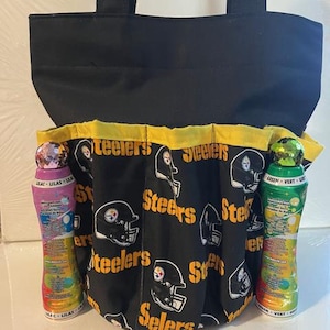 May include: Black tote bag with a Steelers-themed pocket. The pocket features a black fabric with yellow trim, repeating the word "Steelers" and a helmet logo. Two bottles of bubble bath are visible on either side of the pocket.