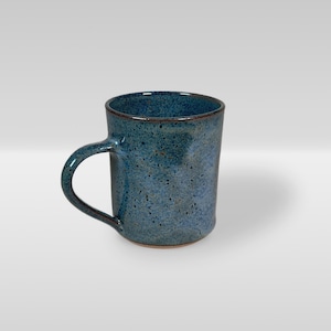 May include: A handmade ceramic mug with a speckled blue glaze. The mug has a rounded handle and a dark brown rim. The mug is approximately 4 inches tall and 3 inches in diameter.