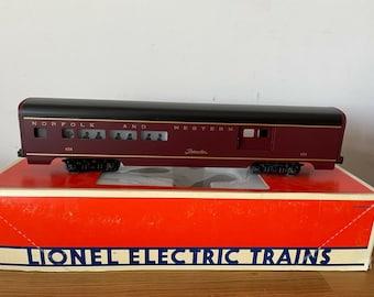 May include: A red and black model train car with the words "Norfolk and Western" printed on the side. The car is sitting on a red box with the words "Lionel Electric Trains" printed on the front.
