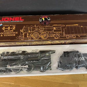 May include: A Lionel large scale 4-4-2 steam locomotive and tender model train set in its original box. The box is brown with gold lettering and features a picture of the train on the front. The train is black with silver accents and has the letters "AT&SF" on the side. The tender has the number "5103" on the side.