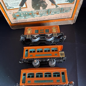 May include: A set of vintage Lionel train carriages in orange and green. The word "OBSERVATION" and "PULLMAN" are visible on the carriages. The background includes a box with the text "LIONEL ACCESSORIES" and "LIONEL MULTIVOLT TRANSFORMERS".