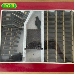 May include: A close-up of a model railway track set in a box. The track is made of plastic and is designed to be used with model trains. The box is red and has the words "L.G.B." printed on it.
