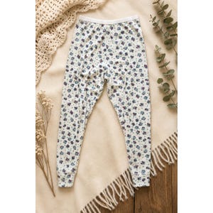 May include: A pair of white leggings featuring a small-scale floral pattern in shades of blue and purple. The leggings have a solid white elastic waistband and matching white ribbed cuffs at the ankles, providing a fitted silhouette.