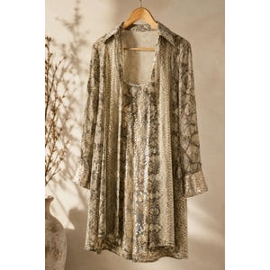 May include: A long-sleeved button-down shirt featuring a beige and black snakeskin print pattern. The garment includes a collar, cuffs adorned with silver sequins, and a matching sequined panel running down the centre front of the shirt.