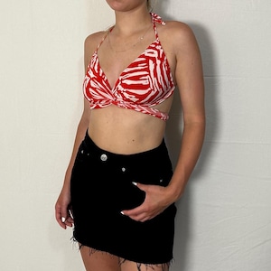 May include: A red and white zebra print halter top with a criss-cross design at the front. The top is worn with a black denim mini skirt.